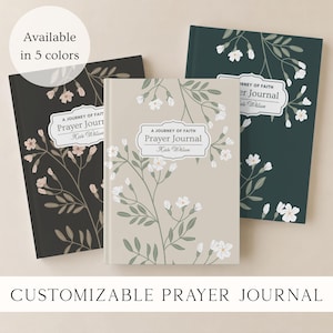 May include: Three hardcover prayer journals with floral illustrations. Each journal features the text A JOURNEY OF FAITH PRAYER JOURNAL Kate Wilson on a white label. The covers are black, beige, and dark green, all decorated with white flowers and green leaves.