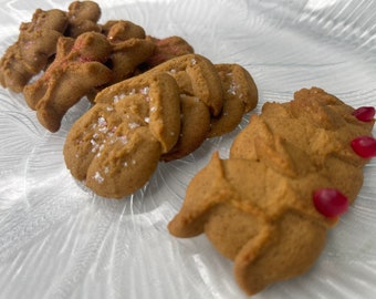 May include: A collection of freshly baked gingerbread cookies on a clear glass plate. The cookies are various shapes, including gingerbread men and leaf shapes, and are decorated with sprinkles and sugar crystals.