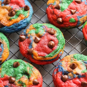 Peut inclure: Gros plan sur des biscuits en spirale arc-en-ciel avec des pépites de chocolat sur une grille métallique. Les biscuits sont rouges, orange, jaunes, verts et bleus.