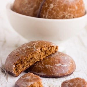 May include: Close-up of gingerbread cookies, some whole and some broken, on a white surface. The cookies are a rich brown color and have a slightly glazed finish.