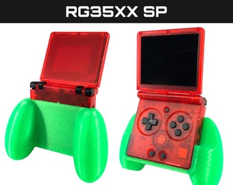 May include: A red and green handheld gaming console with a comfort grip attachment. The console has a screen, buttons, and a D-pad. The grip is made of green plastic and has two large, rounded handles.