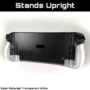 May include: A black handheld gaming device with transparent white grips. The device has buttons, vents, and a screen. The text "Stands Upright" is at the top, and "Color Pictured: Transparent White" is at the bottom.