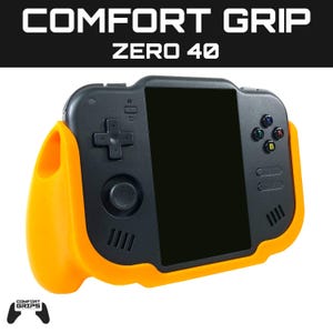 Puede incluir: Consola de juegos portátil negra con una funda Comfort Grip naranja. La consola tiene una pantalla negra, un mando en cruz, botones y el texto "COMFORT GRIP ZERO 40". El logotipo de Comfort Grips está en la esquina inferior izquierda.