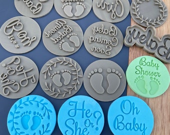 May include: A set of 12 brown, blue, and green cookie cutters with various baby shower themes. The cutters feature phrases like "Oh Baby", "Baby Shower", "He or She?", and "It's a Girl". Some cutters also feature footprints and a wreath design.