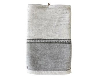 May include: A white and grey kitchen towel with a black stripe and a black and white pattern. The towel is folded and has a loop for hanging.