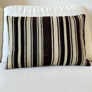 Peut inclure: Un coussin de canapé rayé marron et blanc avec une texture tissée.