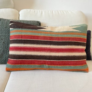 Peut inclure: Un coussin de canapé rayé avec un motif de couleurs brun, rouge, vert et orange. Le coussin est fait d'un tissu tissé et a une forme rectangulaire.