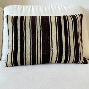 Peut inclure: Un coussin rayé avec des rayures brunes et blanches. Le coussin est fait d'un tissu tissé et a une forme rectangulaire.