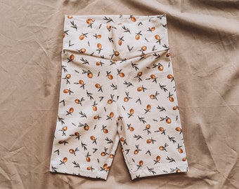May include: White bike shorts with a lemon print. The shorts have a high waist and are made of a soft, stretchy fabric.