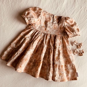 May include: A tiered floral print dress with puffed sleeves and a square neckline. The dress is made of a lightweight fabric and has a relaxed fit.