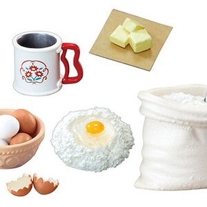 May include: A set of miniature baking supplies, including a bag of flour, a scoop, a bowl of eggs, a cup of milk, a stick of butter, and a bowl of batter with an egg yolk in the center.