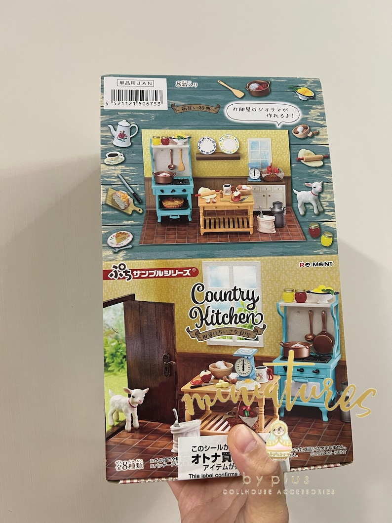 May include: A box for a miniature dollhouse kit featuring a country kitchen. The box is blue and green with a picture of a miniature kitchen on the front. The text on the box reads "Country Kitchen" and "Re-ment".