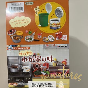 Puede incluir: Una caja de miniaturas de alimentos para casas de muñecas. La caja es naranja y blanca con texto japonés. El texto en la caja dice "Comidas caseras". La caja contiene 8 miniaturas de alimentos, incluyendo una olla arrocera, una sartén, una olla y un cubo de basura.