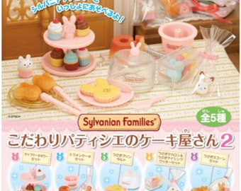 May include: A set of five Sylvanian Families miniature bakery playsets. Each set features a different type of cake or pastry, including cupcakes, a cake with a cherry on top, a tart, a pudding, and a croissant. The sets are packaged in clear plastic bags with a pink and white label that says "Sylvanian Families" and "こだわりパティシエのケーキ屋さん2".