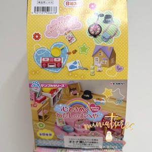 May include: A box of miniature dollhouse accessories. The box features illustrations of miniature furniture, a house, a unicycle, and other small toys. The box has Japanese text and is decorated with stars, hearts, and flowers. The box is yellow and pink.