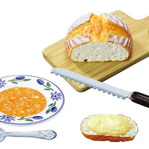 May include: A miniature kitchen set with a loaf of bread on a wooden cutting board, a serrated knife, a plate with orange jam, a spoon, and a slice of bread with butter.
