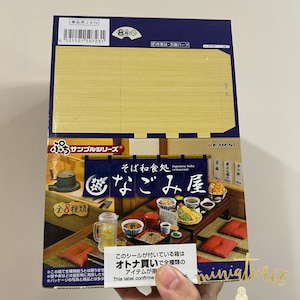 Könnte beinhalten: Eine Schachtel für ein japanisches Soba-Restaurant-Miniaturset. Die Schachtel zeigt eine farbenfrohe Illustration eines Restaurant-Innenraums mit Tischen, Stühlen und Essen. Der Text auf der Schachtel lautet "Japanisches Soba-Restaurant" und "Nagomi-ya".