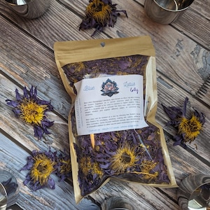 Pode incluir: Um pacote de flores de lótus azuis com o texto "Blue Lotus 60g" e uma ilustração de flor de lótus. Flores de lótus azuis secas e xícaras de prata dispostas sobre uma superfície de madeira.