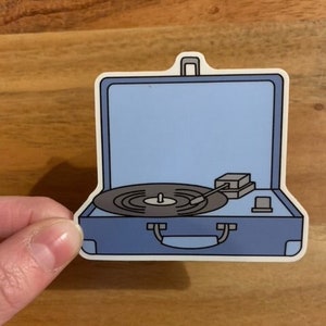 May include: A blue and white portable record player with a black vinyl record on the turntable. The record player has a handle on the top and a small speaker on the side.