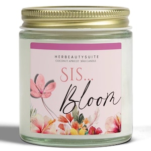 Può includere: Candela in barattolo di vetro con coperchio dorato. L'etichetta è rosa con le parole "SIS... Bloom" in corsivo. L'etichetta include anche illustrazioni floreali e il testo "HERBEAUTYSUITE COCONUT APRICOT WAX CANDLE."