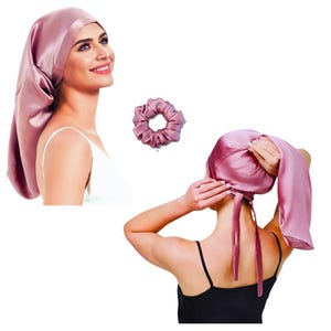 May include: A pink satin sleep cap with a tie closure. The cap is designed to protect hair from breakage and frizz while sleeping. A matching pink satin scrunchie is also shown.