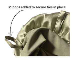 May include: Close-up of a sage green satin bonnet with two loops to secure ties. The text "2 loops added to secure ties in place" is visible. The bonnet is made of a soft, shiny fabric.