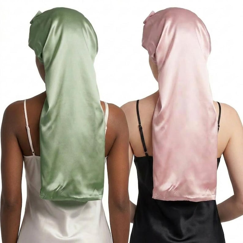 May include: Two satin hair bonnets, one in a soft sage green and the other in a delicate blush pink. The bonnets are long, covering the back of the neck, and tied at the top. The models are wearing satin camisoles.