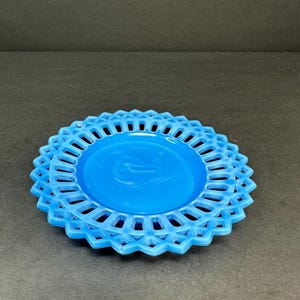 Puede incluir: Un plato de vidrio azul claro con un borde decorativo festoneado. El plato tiene un diseño delicado y calado.