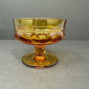 May include: A vintage amber glass footed bowl with a textured design. The bowl has a scalloped rim and a pedestal base.