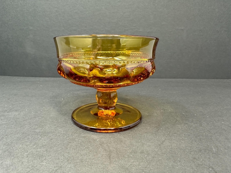 May include: A vintage amber glass footed bowl with a textured design. The bowl has a scalloped rim and a pedestal base.