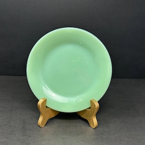 Peut inclure: Une assiette en verre vert clair avec un bord légèrement surélevé. L'assiette est sur un support en bois.