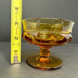 May include: Amber glass dessert dish with a scalloped rim and a pedestal base. The dish has a textured pattern of small circles.