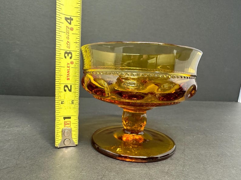 May include: Amber glass dessert dish with a scalloped rim and a pedestal base. The dish has a textured pattern of small circles.