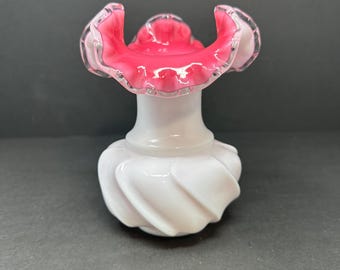 May include: A white milk glass vase with a pink ruffled top. The vase has a swirl design.