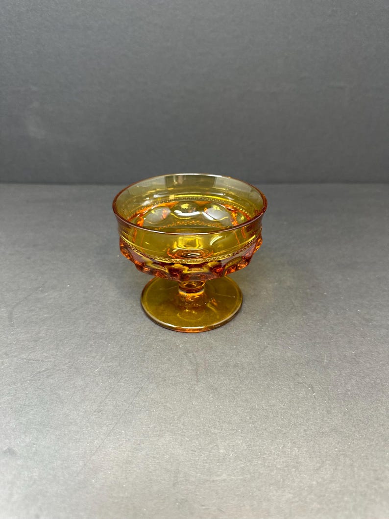 May include: A small amber glass goblet with a textured design and a short stem. The goblet is ideal for serving small portions of dessert or drinks.