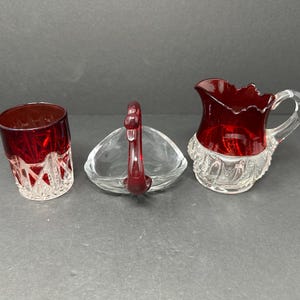 May include: Three glass pieces with a ruby red interior and clear cut glass exterior. A small glass cup, a small swan-shaped dish, and a small pitcher.