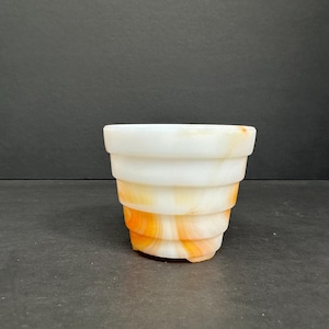 Puede incluir: Un macetero de cerámica blanco y naranja con vetas de mármol y diseño acanalado. El macetero mide aproximadamente 10 cm de alto y 7,5 cm de ancho.