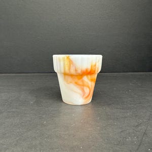May include: A white and orange swirl glass planter with a fluted rim.