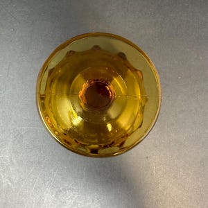 May include: Amber glass goblet with a scalloped rim and a thick base. The goblet is empty and appears to be vintage.