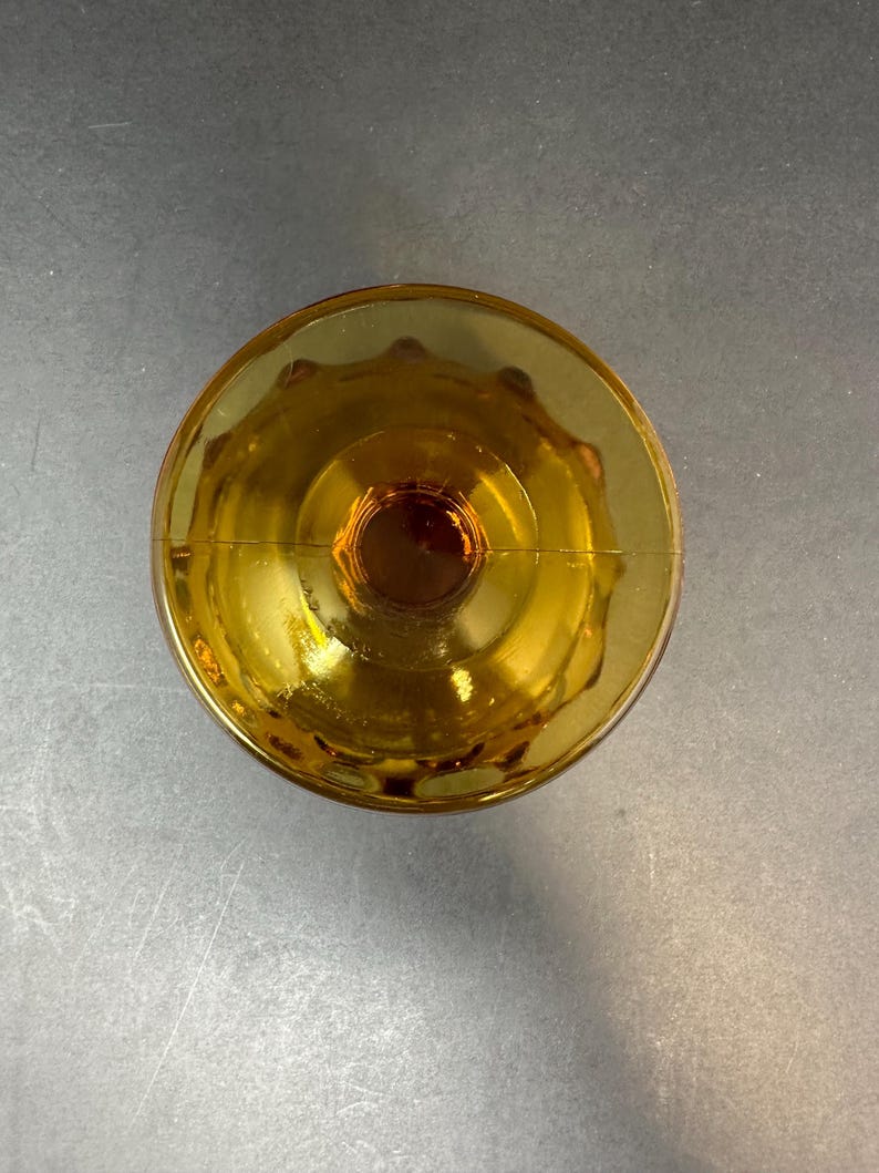 May include: Amber glass goblet with a scalloped rim and a thick base. The goblet is empty and appears to be vintage.
