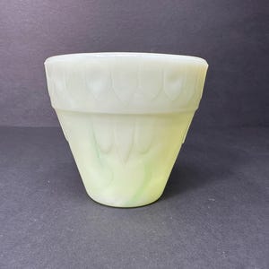 Puede incluir: Un macetero de vidrio blanco y verde con un borde festoneado y un diseño floral.