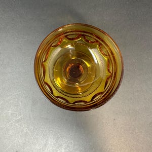 May include: A clear amber glass bowl with a decorative pattern around the rim. The bowl has a small, round base.