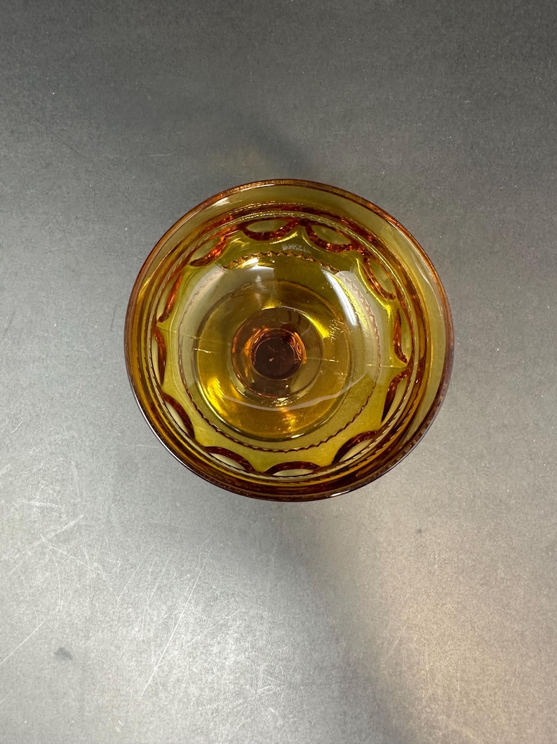 May include: A clear amber glass bowl with a decorative pattern around the rim. The bowl has a small, round base.