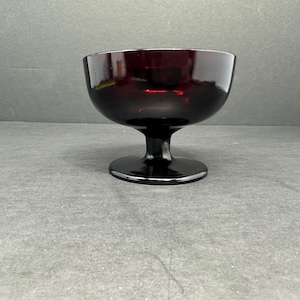 May include: A dark red glass pedestal bowl with a wide, round base.