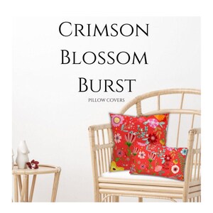 May include: Two red floral pillow covers, one square and one rectangular, rest on a wicker chair. The pillows feature a vibrant mix of flowers in pink, yellow, and white. The text "CRIMSON BLOSSOM BURST PILLOW COVERS" is at the top.