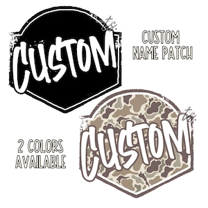 Può includere: Sono presentati due modelli di toppe personalizzate con nome. Uno è nero con testo bianco, l'altro è un motivo mimetico con testo bianco. Il testo "CUSTOM" è in grassetto, in stile scritto a mano. Vengono visualizzati anche i testi "CUSTOM NAME PATCH" e "2 COLORI DISPONIBILI".