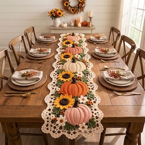 Puede incluir: Un camino de mesa largo de ganchillo color crema con un patrón repetitivo de calabazas tridimensionales en tonos naranja, rosa y blanco, intercaladas con girasoles, pequeñas flores blancas y hojas verdes tejidas a ganchillo.