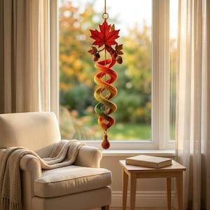 May include: A hanging spiral ornament featuring a gradient of colors from red at the top to green at the bottom. The top is adorned with a large red maple leaf and two small acorns. A small, textured, round, orange-brown weight hangs at the bottom.