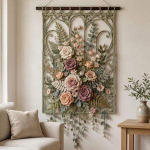 May include: A rectangular wall hanging featuring an intricate sage green crocheted lattice frame. The center is adorned with a dense arrangement of crocheted flowers in shades of dusty rose, mauve, and cream, interspersed with detailed fern leaves.
