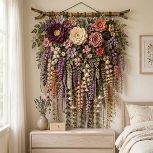 May include: A large wall hanging featuring an intricate arrangement of crocheted flowers and foliage in shades of purple, pink, cream, and green. The botanical display is suspended from a natural wooden branch with a thin cord for mounting.